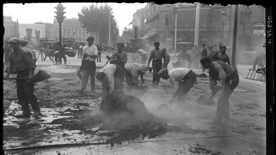 Historic black and white photo of workers paving Rambla de Catalunya near Gran Via in 1928, with old buildings in the backgro