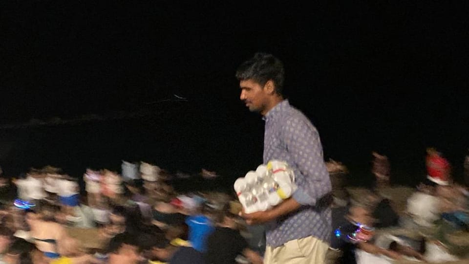 A street vendor selling cans of beer in a busy Barcelona square at night.