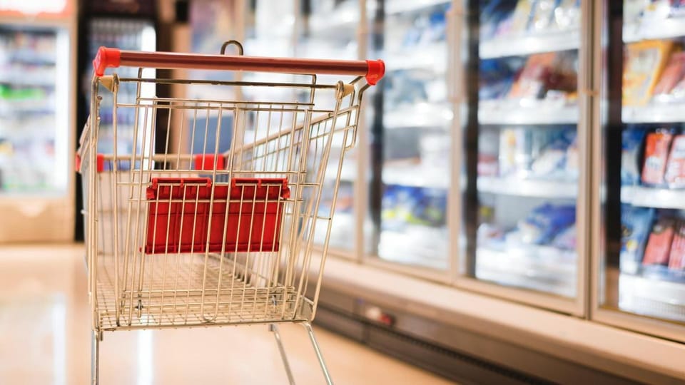A closed supermarket entrance with a sign indicating holiday hours, showing empty shopping trolleys outside.