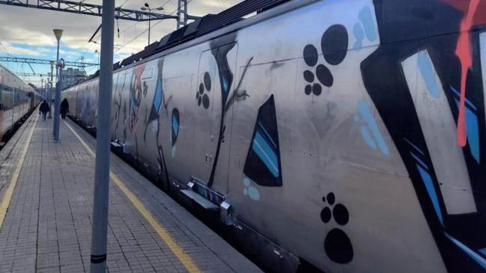 Catalan police officers inspecting a graffiti-covered train carriage at a Barcelona railway depot.