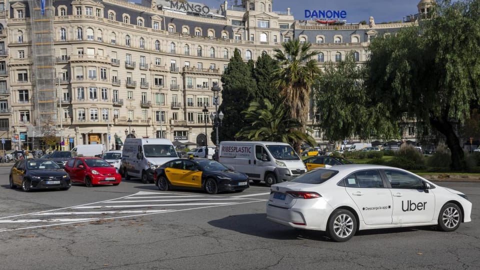 VTC vehicles driving on a street in Barcelona, with a taxi in the background.