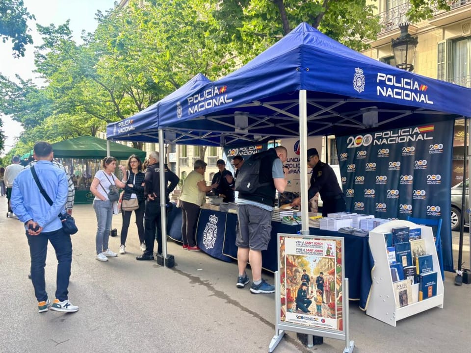 A street scene in Barcelona during Sant Jordi, with people browsing book and rose stalls, possibly on Rambla de Catalunya.
