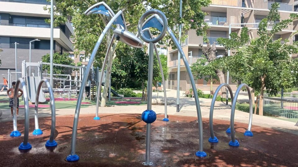 Children playing in a modern water jet park with anti-slip flooring and various water features in a city setting.
