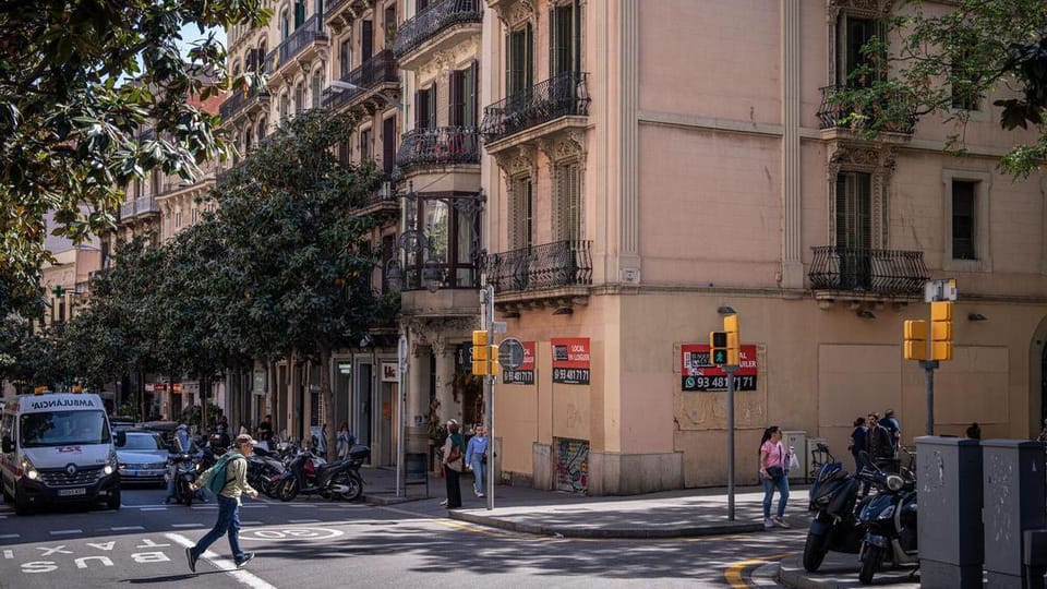 A commercial property on a street corner in Barcelona's Gràcia district, with wooden boards covering its windows and 'For Ren