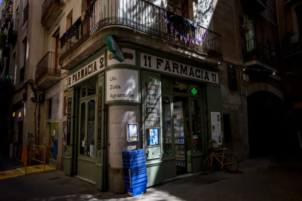 Exterior view of Farmàcia Agramonte, a historic Barcelona pharmacy with green wooden doors and engraved glass windows.