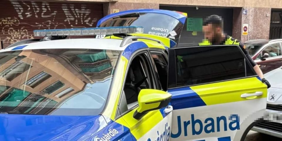 Police vehicle parked outside a building on a street in L'Hospitalet de Llobregat, with a closed metal shutter on the ground 