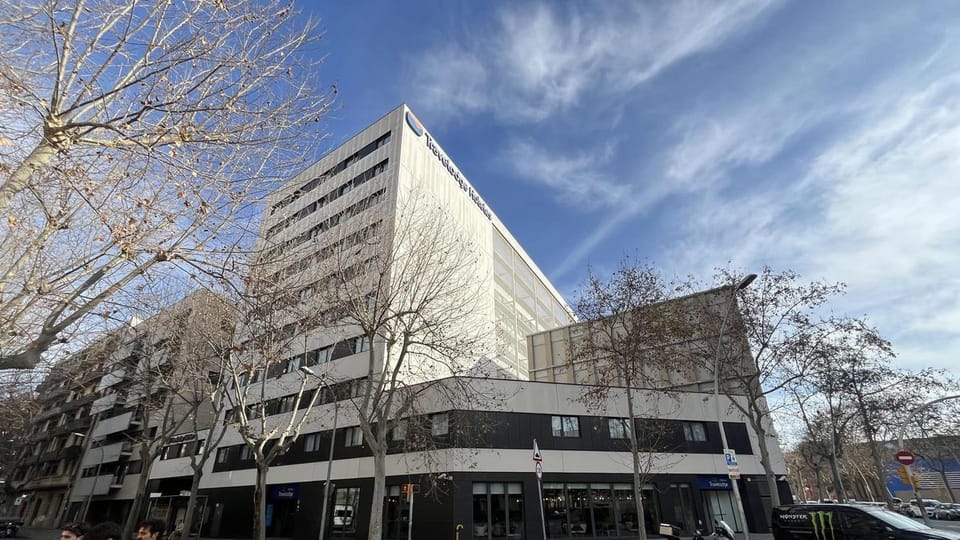 Exterior view of the Travelodge Poblenou hotel in Barcelona, a modern building with a blue and white facade under a clear sky