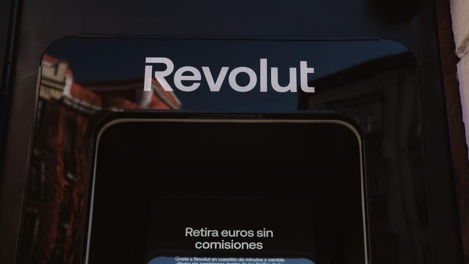 Revolut logo on a modern building facade in Barcelona, with people walking past.