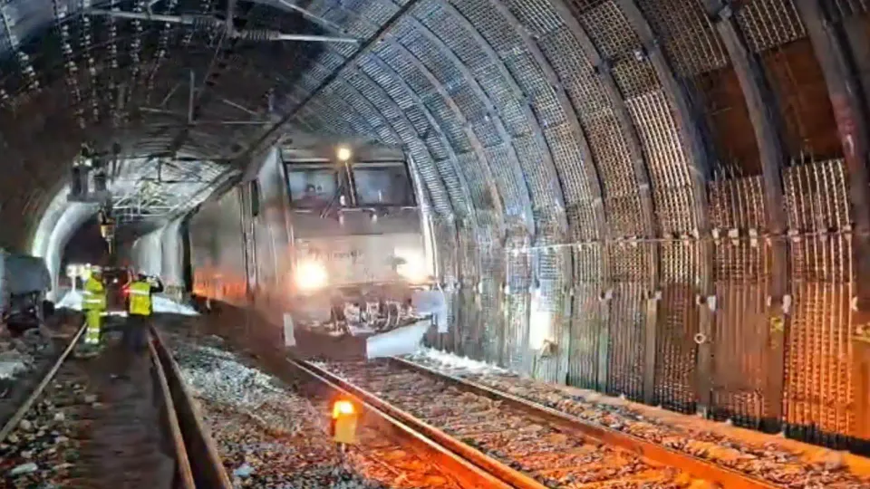 A freight train travelling through a tunnel, with visible reinforcement structures on the tunnel walls.