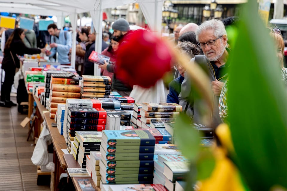 People browsing books and buying roses at a Sant Jordi stall on a busy street in Barcelona.