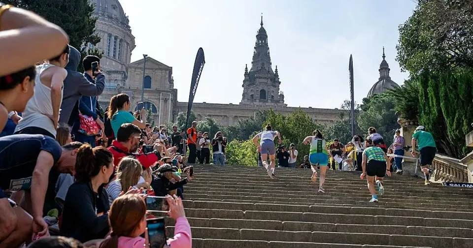 Runners ascend a steep staircase on Montjuïc mountain with Barcelona city views in the background during the Salomon Run.