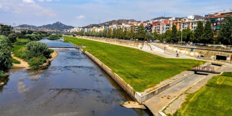 An aerial view of Parc Fluvial del Besòs, showing green spaces, walking paths, and the Besòs River winding through an urban a