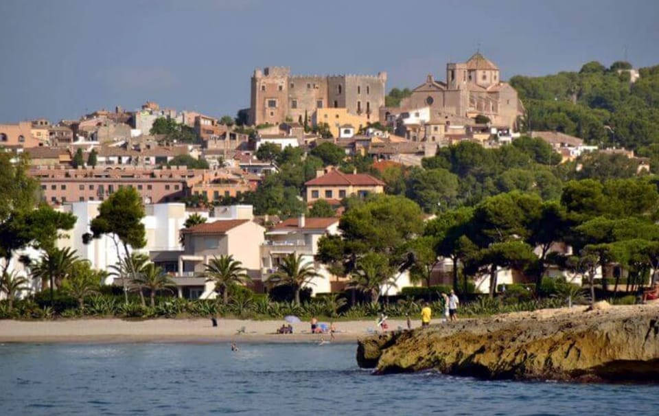 View of Altafulla's medieval Vila Closa with its stone buildings and the castle tower rising above, under a clear sky.