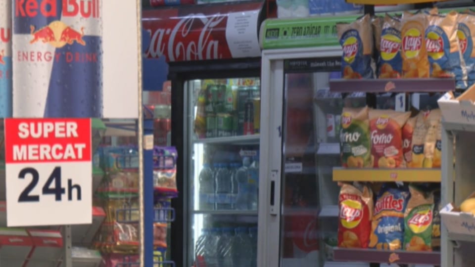 A brightly lit 24-hour convenience store with a prominent sign, located on a busy street in Barcelona at night.