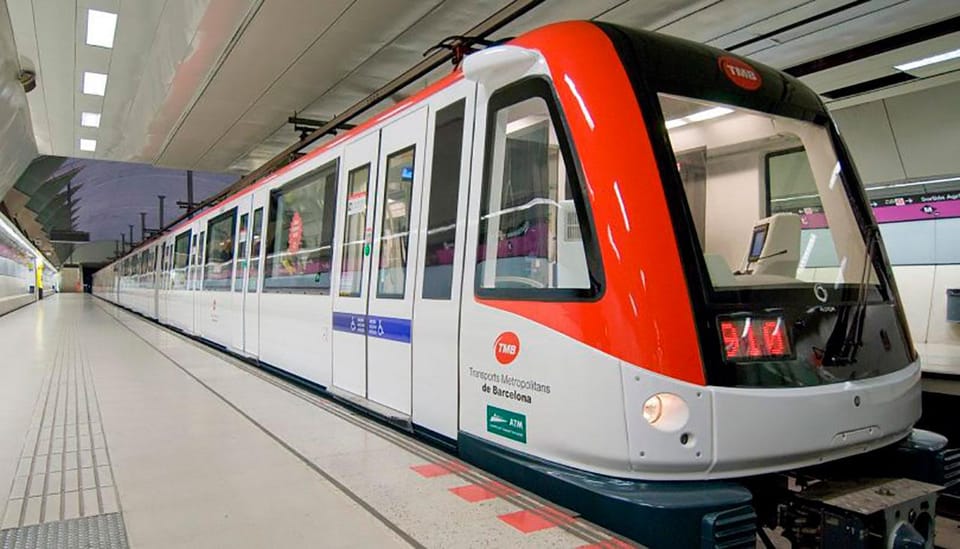 A crowded Barcelona Metro train carriage with diverse passengers standing and sitting.