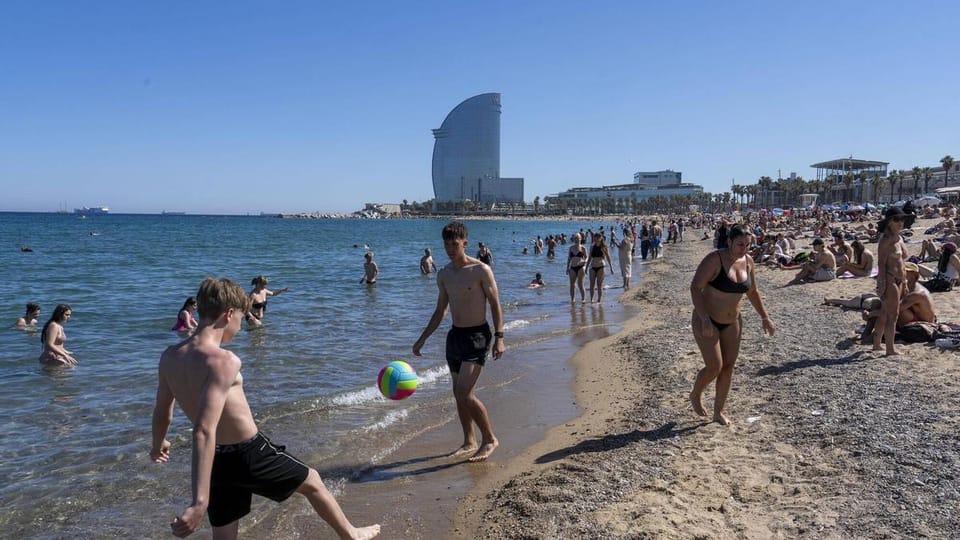 A clean, sandy beach in Barcelona with clear blue water and a few people enjoying the sun, showing no signs of litter or smok