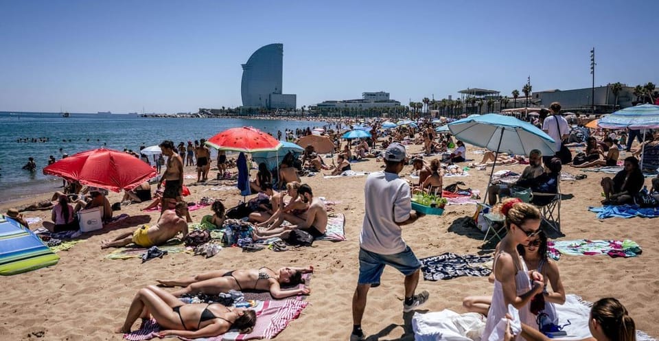 People relaxing on Bogatell beach in Barcelona, with parasols, towels, and the sea in the background.