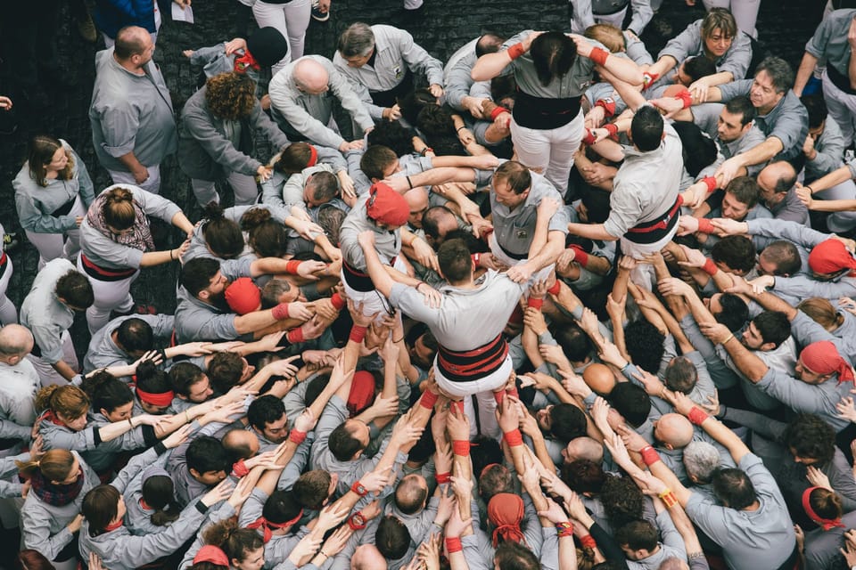 A tall human tower, or castell, being built by a group of people in a public square in Barcelona, with spectators watching.