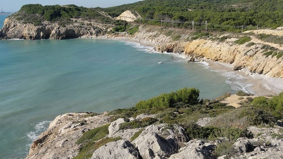 A picturesque cove with clear blue water, sandy beach, and green cliffs, with a train passing in the background.