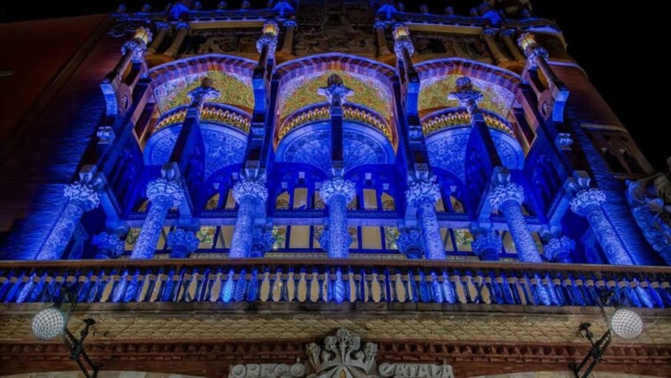 The Museu del Disseny de Barcelona (DHub) building illuminated in blue, with a large European Union flag unfurled in Plaça de