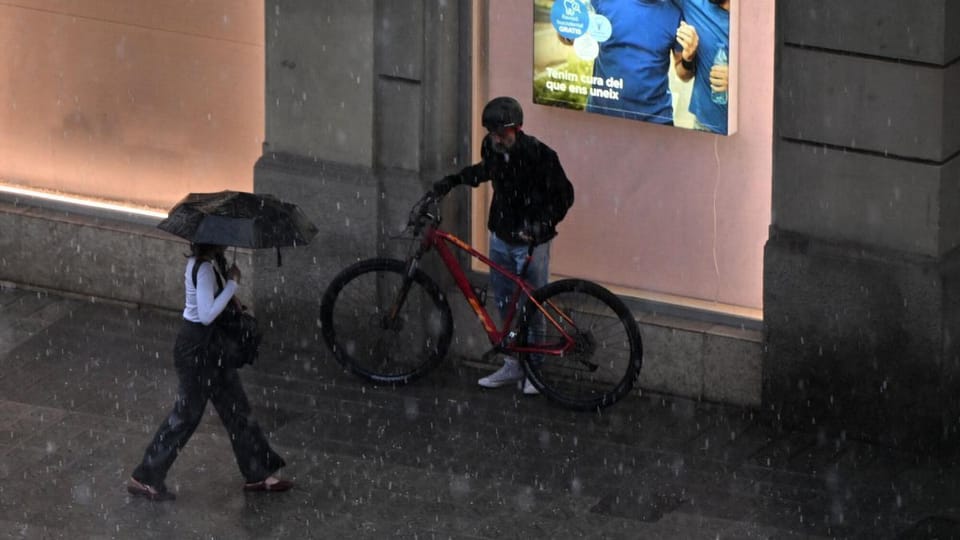 Hailstones covering a street in Barcelona after a severe storm, with wet pavements and buildings in the background.
