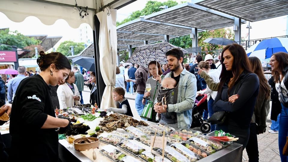 A bustling outdoor market scene at Plaça de les Glòries Catalanes, with various stalls, people browsing, and a festive atmosp