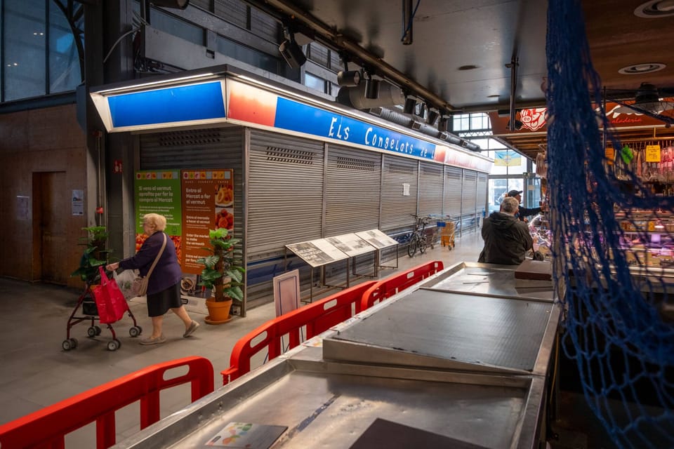 Empty stalls and a few active vendors inside a traditional Barcelona municipal market with high ceilings and natural light.