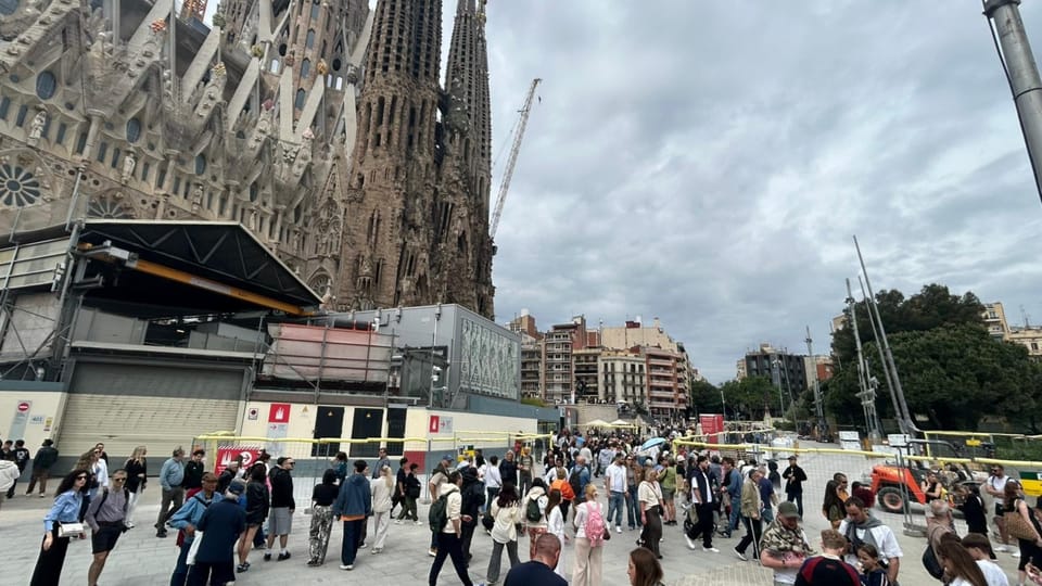 Crowds of people gather outside the Sagrada Familia in Barcelona on a sunny day.