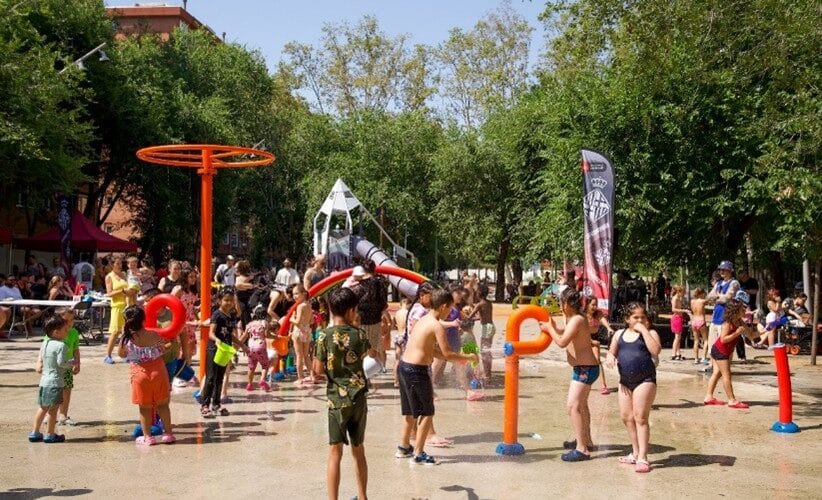 Children playing in a splash pad with water jets in a public park in Barcelona.