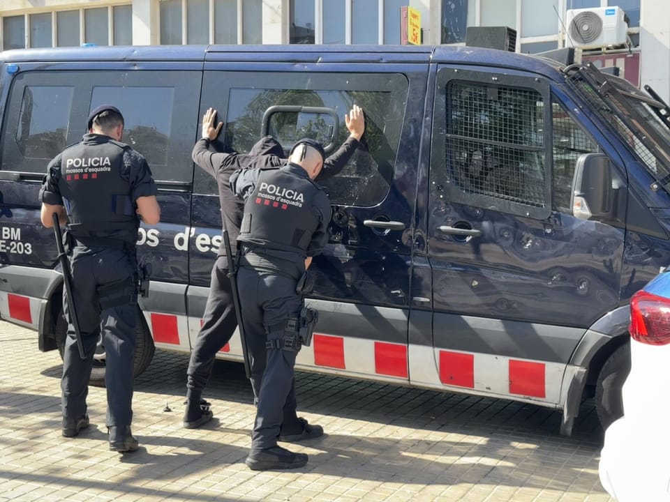 Mossos d'Esquadra officers on patrol in a busy Barcelona street, with historic buildings in the background.
