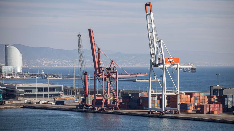 Aerial view of the Port of Barcelona with cargo ships, containers, and cranes under a clear sky.