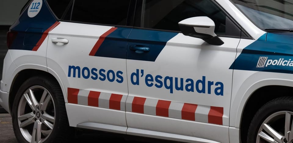 A Mossos d'Esquadra police car parked near a school building in Barcelona, with students visible in the background.