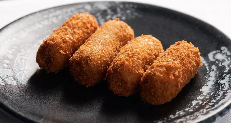 A close-up of a 'Barceloneta bomba' dish with aioli and bravas sauce, served on a white plate in a restaurant setting.