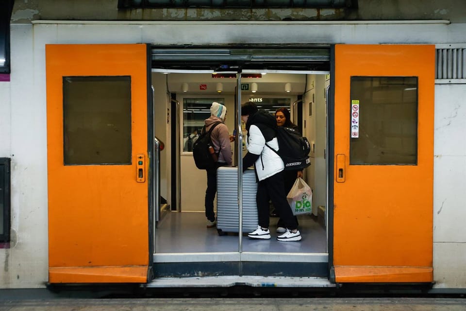 A Rodalies train arriving at a platform in a Barcelona train station, with passengers waiting.