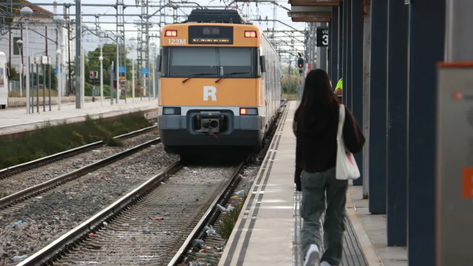 A Rodalies train arriving at a station platform in Barcelona, with passengers waiting to board.