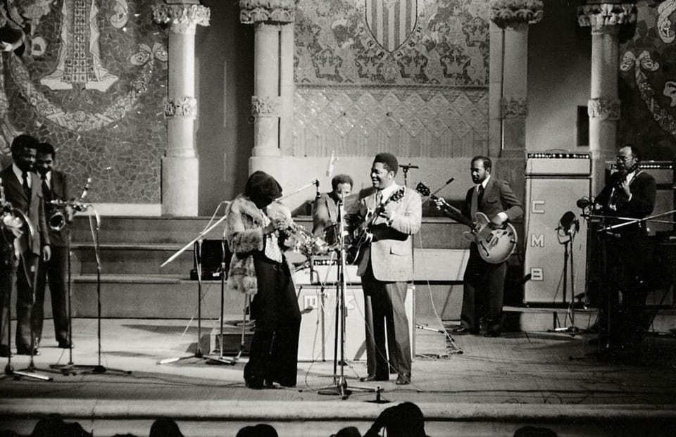 Miles Davis playing trumpet on stage, spotlight on him, audience in background.