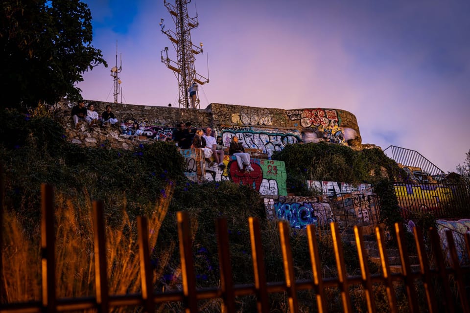 People gathered at the Turó de la Rovira viewpoint in Barcelona, with the city skyline visible at dusk.