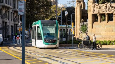 A modern yellow and white Trambesòs tram travels along tracks in Barcelona's urban area.