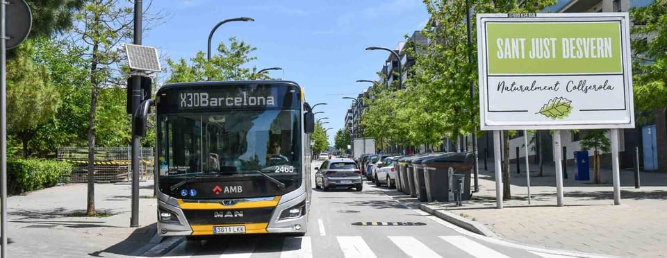 A new 18-metre articulated hybrid bus, painted in red and white, drives on a city street in Barcelona.