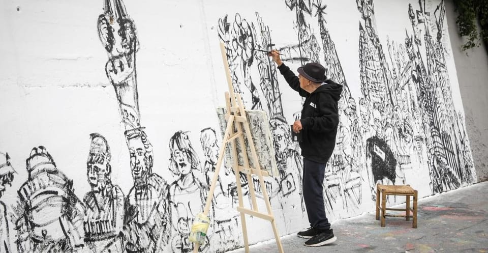 Joan Bueno, a 93-year-old artist, stands proudly next to his newly completed 17-metre mural at BesArt, depicting everyday Bar